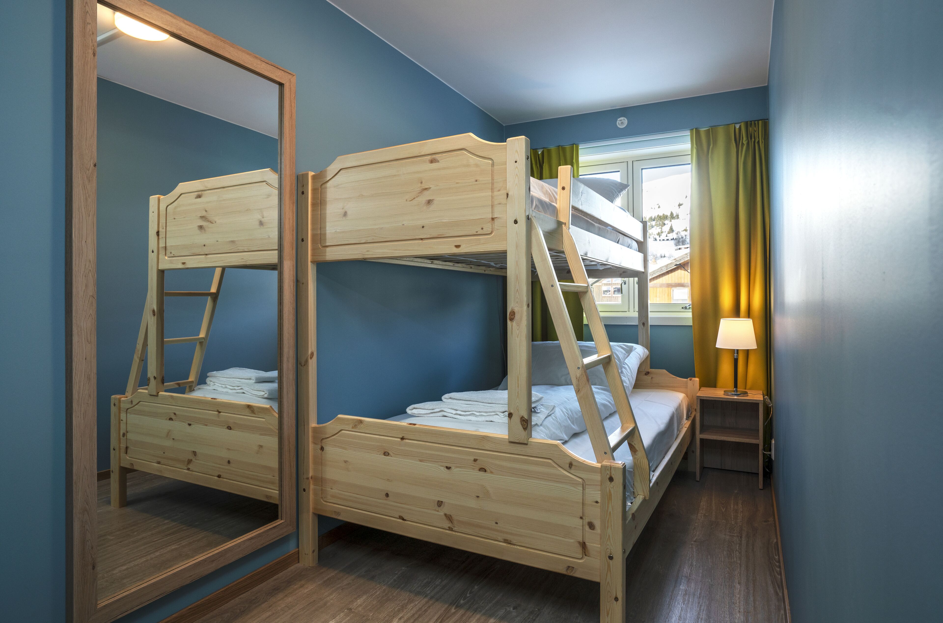 A room with two bunk beds, a small bedside table with a lamp, and a window with curtains.
