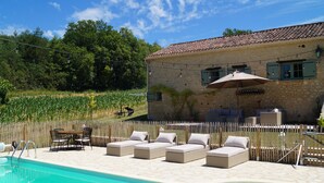 A stone building with a tiled roof, outdoor seating, and a swimming pool.