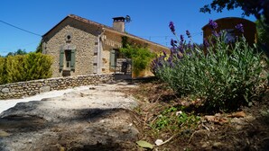 A stone house with a tiled roof, a chimney, and a small window.