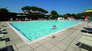 A swimming pool with lounge chairs and umbrellas, surrounded by trees and buildings. - Tidy Chalet with Terrace near Sea (Ravenna)
