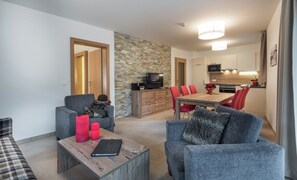 A modern living room with grey sofas, a wooden coffee table, and a red vase. A television is on a wooden cabinet, and a stone wall separates the living room from the kitchen. - Apartment in Zell am See Near the ski Area (Zell am See)