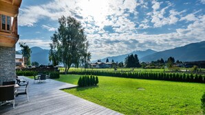 A wooden deck with outdoor furniture, a grassy lawn, and a view of mountains and houses in the background. - Apartment in Zell am See Near the ski Area (Zell am See)
