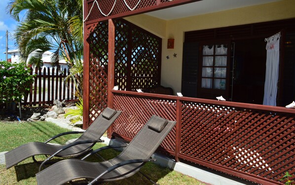 A covered outdoor seating area with two lounge chairs, a wooden lattice partition, and a door with a window.