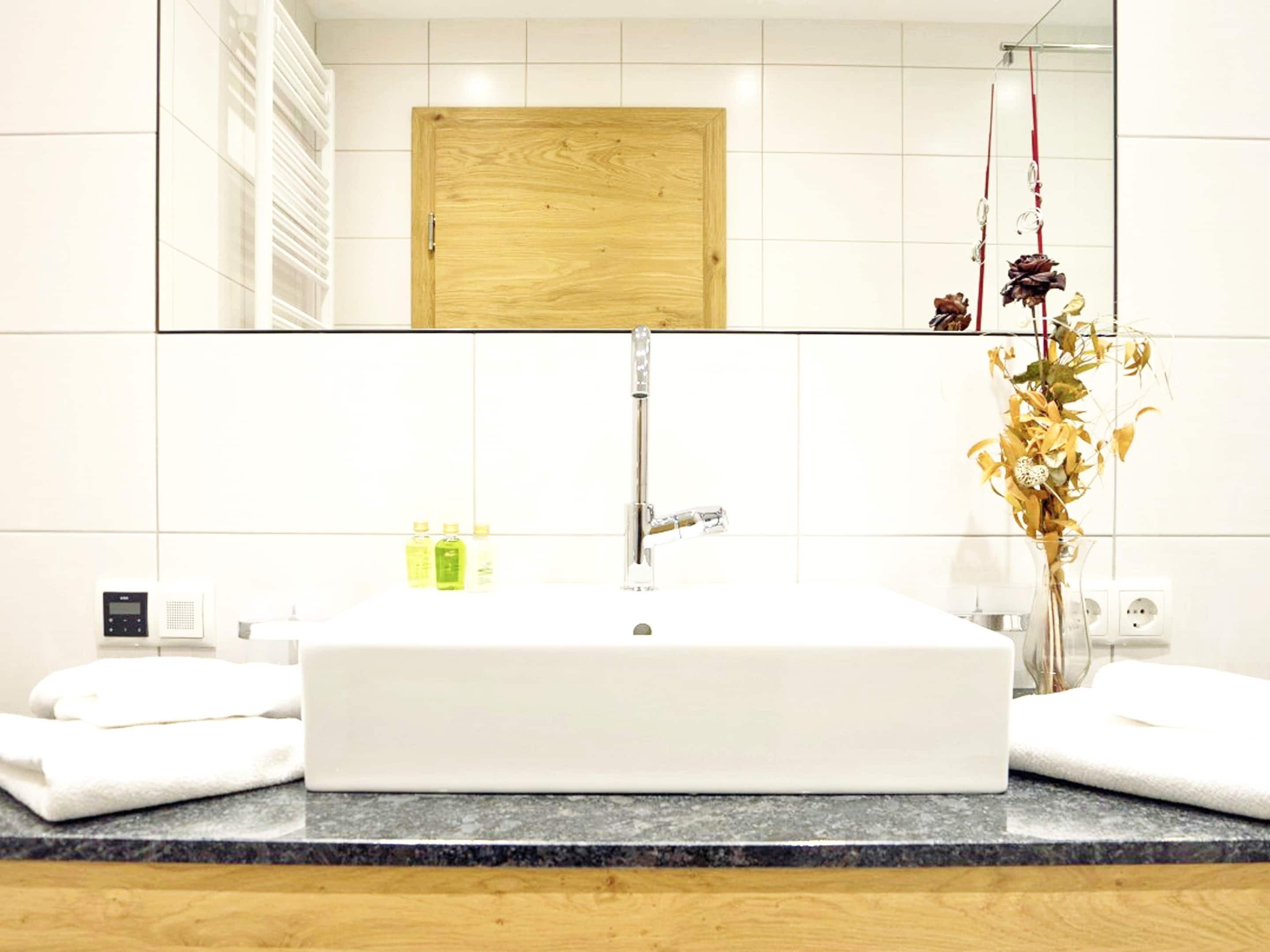 A modern bathroom with a rectangular sink, a wooden door, and a vase with dried flowers.