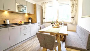 A modern kitchen with a dining area, wooden cabinets, a coffee maker, and a window with curtains. - Chalet in Mayrhofen Near Ski Lifts (Schwendau)