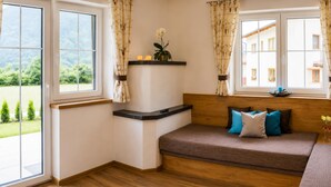 A room with a wooden floor, a brown sofa with blue and white cushions, a small table with candles, and a window with curtains. - Chalet in Mayrhofen Near Ski Lifts (Schwendau)