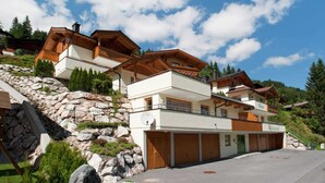 Un chalet à plusieurs étages, doté d’une façade en pierre, de balcons en bois et d’un garage.