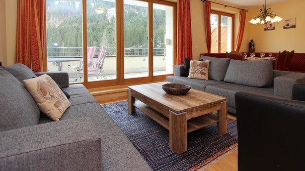 Un salon moderne avec un canapé gris, une table basse en bois et une vue sur un balcon agrémenté de rideaux rouges.