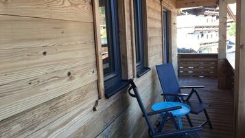 A wooden cabin with a porch, two chairs, and a window.