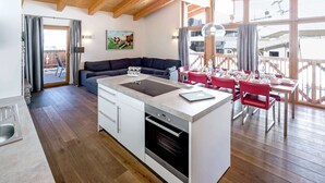Una cocina moderna con una isla central, suelo de madera y una zona de comedor con sillas rojas.