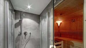 Un baño moderno con ducha envuelta en vidrio, sauna de madera y un perchero visible.