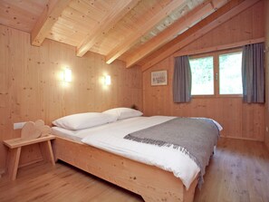 Une chambre dans une cabane en bois, avec un lit, une table de chevet et une fenêtre avec des rideaux.