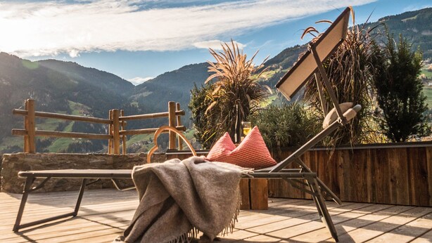 Un fauteuil suspendu en forme de hamac, avec une couverture, une clôture en bois et une vue sur les montagnes et la verdure.