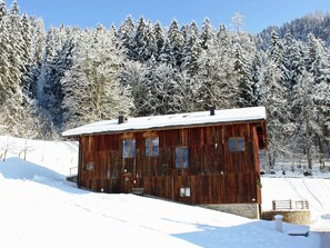 Une cabane en bois rustique, dont le toit est recouvert de neige, entourée d’une forêt d’arbres chargés de neige.