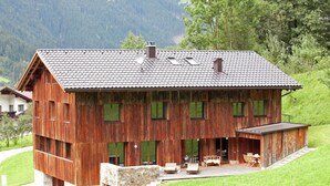 Une maison rustique en bois, avec des fondations en pierre, de grandes fenêtres et un balcon doté de meubles pour se détendre en plein air.