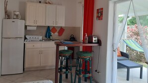 A compact kitchen with white cabinets, a refrigerator, a gas stove, and a small dining area with stools. -  Tropical Gecko Studio - Only 80 meters from the Ocean! (Silver Sands)