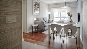 A modern living room with a grey sofa, a round coffee table, and a dining area with white chairs and a table. - Be Bop by FeelFree Rentals (Donostia)