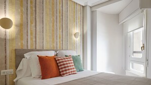 A neatly made bed with white linens and multiple pillows, a striped wall with a textured pattern, and a window with a view of the outside. - Be Bop by FeelFree Rentals (Donostia)