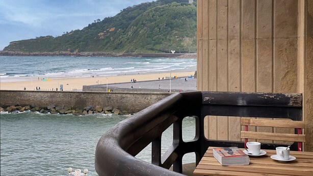 A seaside view from a balcony with a wooden table, chairs, and a book. - Be Bop by FeelFree Rentals (Donostia)
