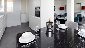 A modern kitchen with white cabinets, a built-in oven, and a dining area with a black marble table set for four. - Playa de La Concha 7 by FeelFree Rentals (Donostia)
