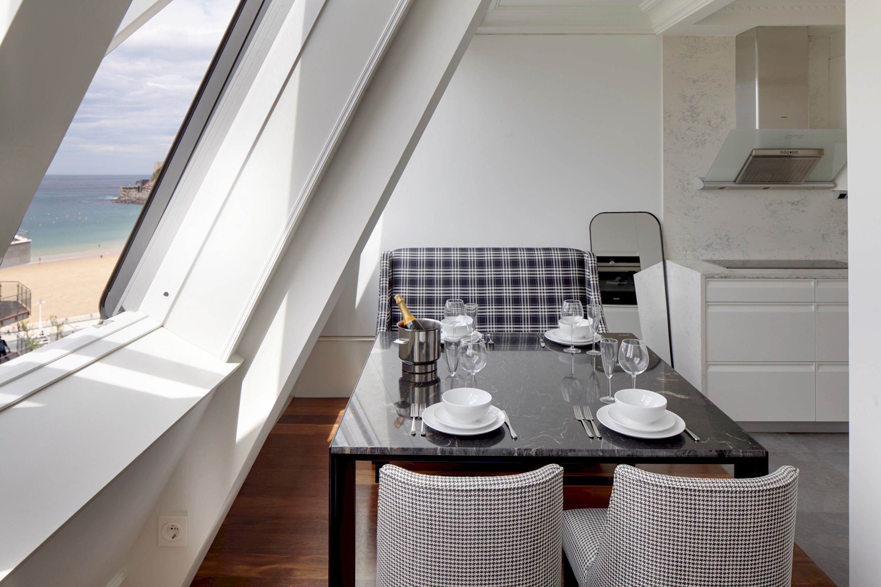 Un comedor con mesa lista para cuatro, vista a la playa y zona de cocina.