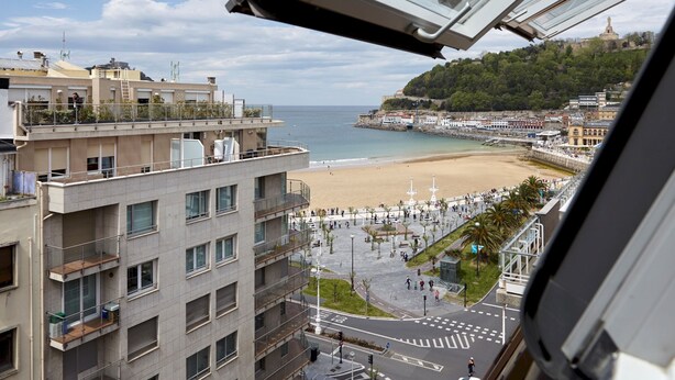 A view of a beach with a promenade, buildings, and a distant hill with a tower. - Playa de La Concha 7 by FeelFree Rentals (Donostia)