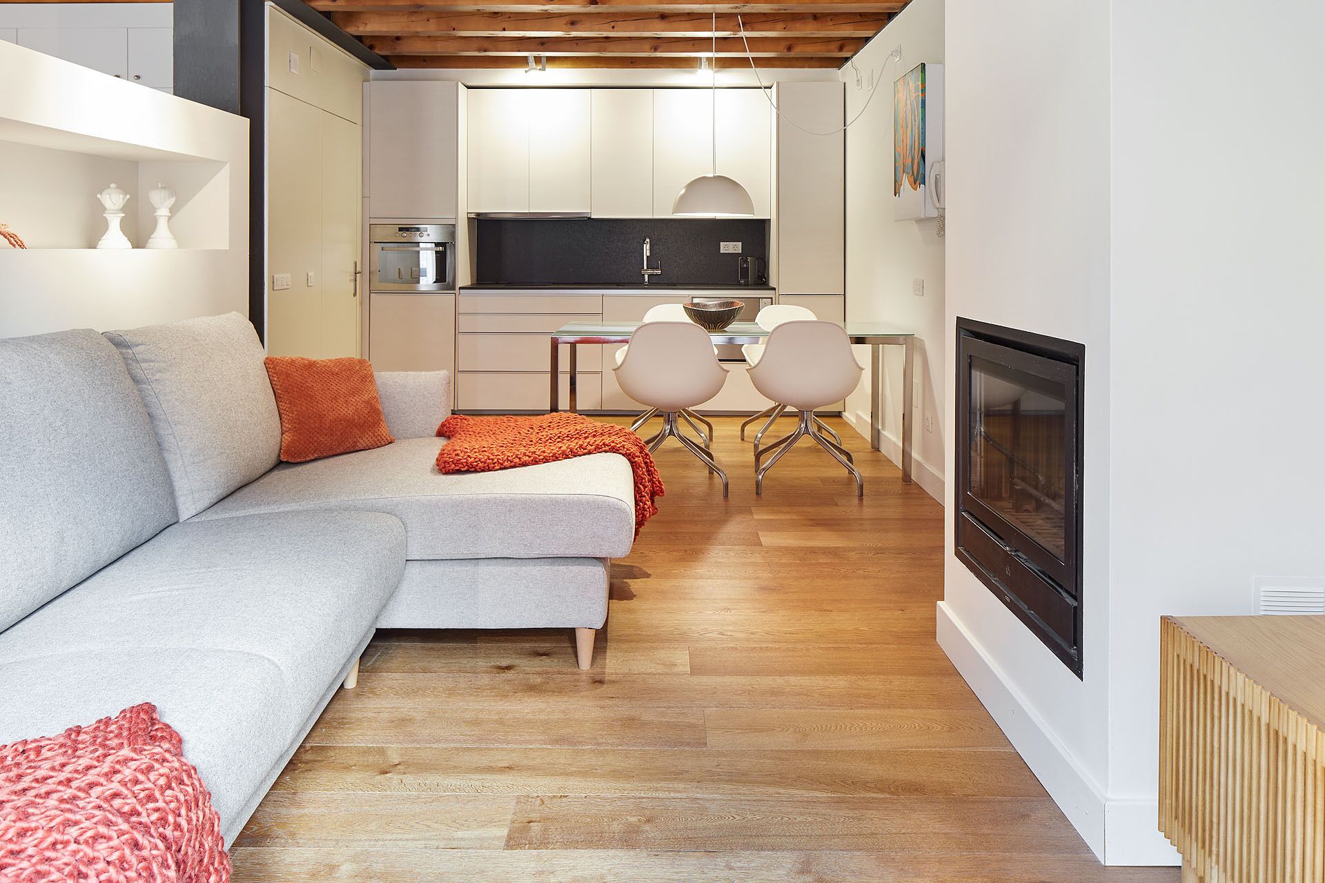 Un salon moderne avec un canapé gris, un plaid orange et une cheminée.