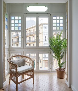 A room with large windows, a wicker chair, and a potted plant. - Easo Suite 2B by FeelFree Rentals (Donostia)