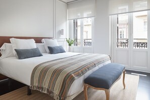 A neatly made bed with a striped blanket and pillows, a wooden bench, and a view of a balcony with a railing. - Pitipombo by FeelFree Rentals (Donostia)