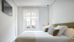 A hotel room with a large bed, a bedside table, a lamp, and a window with a view of buildings. - Pitipombo by FeelFree Rentals (Donostia)
