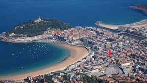 Eine Luftaufnahme einer Küstenstadt mit einer markanten Festung auf einem Hügel, einem Sandstrand und einem dicht bebauten Stadtgebiet mit zahlreichen Gebäuden.