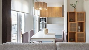 Eine moderne Küche mit Einbauofen und Kühlschrank, ein Essbereich mit weißem Tisch und Stühlen sowie ein Holzregal.
