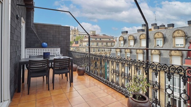 Ein Balkon mit Tisch und Stühlen, einem Blumentopf und Blick auf die umliegenden Gebäude.