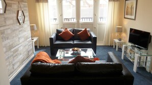 A living room with a black sofa, a glass coffee table, and a television on a glass cabinet. - The Sawmills (Carlisle)