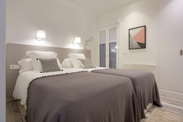 Un dormitorio moderno con dos camas, un ventanal grande y una obra de arte colgada en la pared.