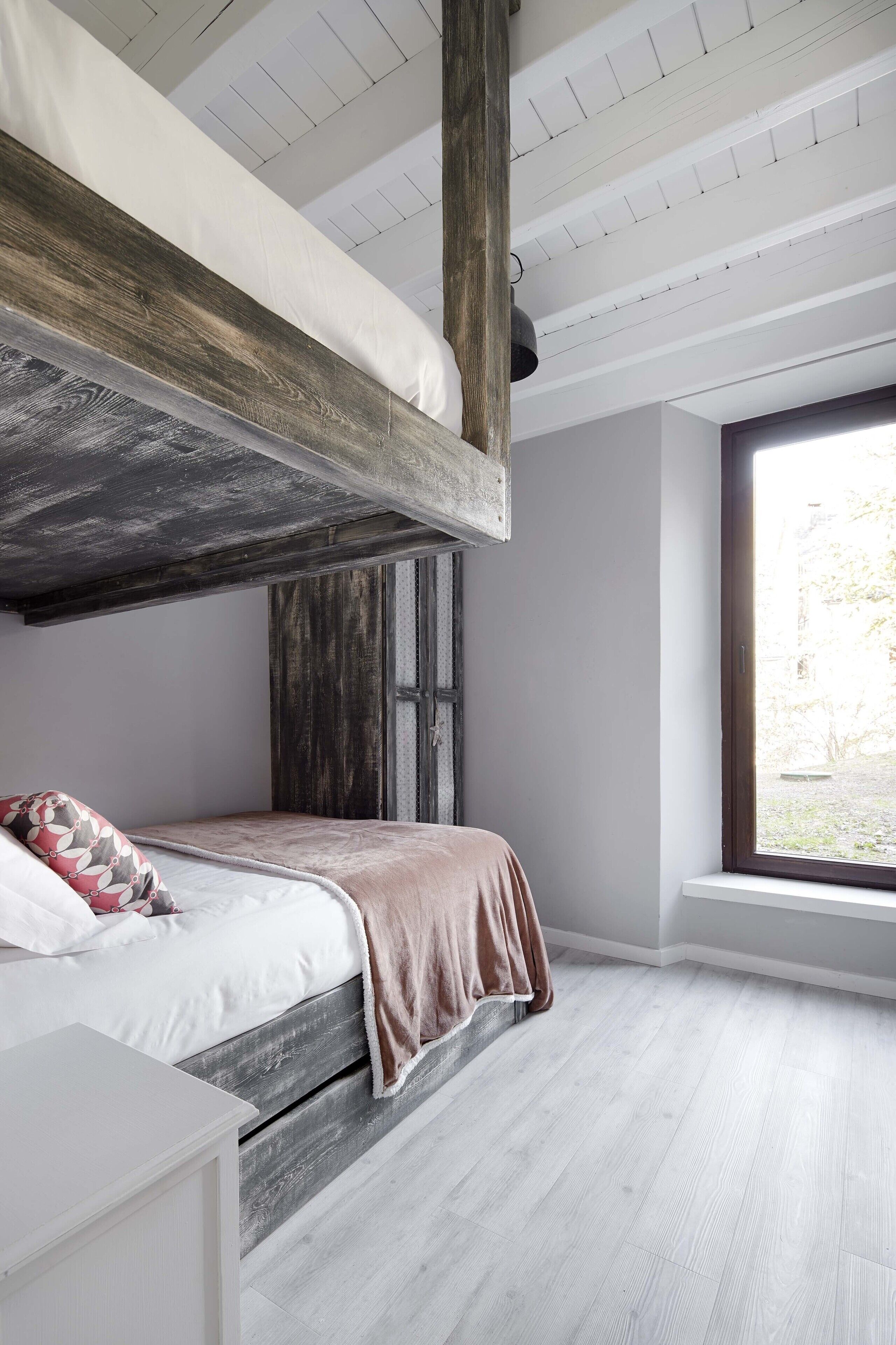 A bunk bed with a wooden headboard, a bedside table, and a window with a view of the outdoors.
