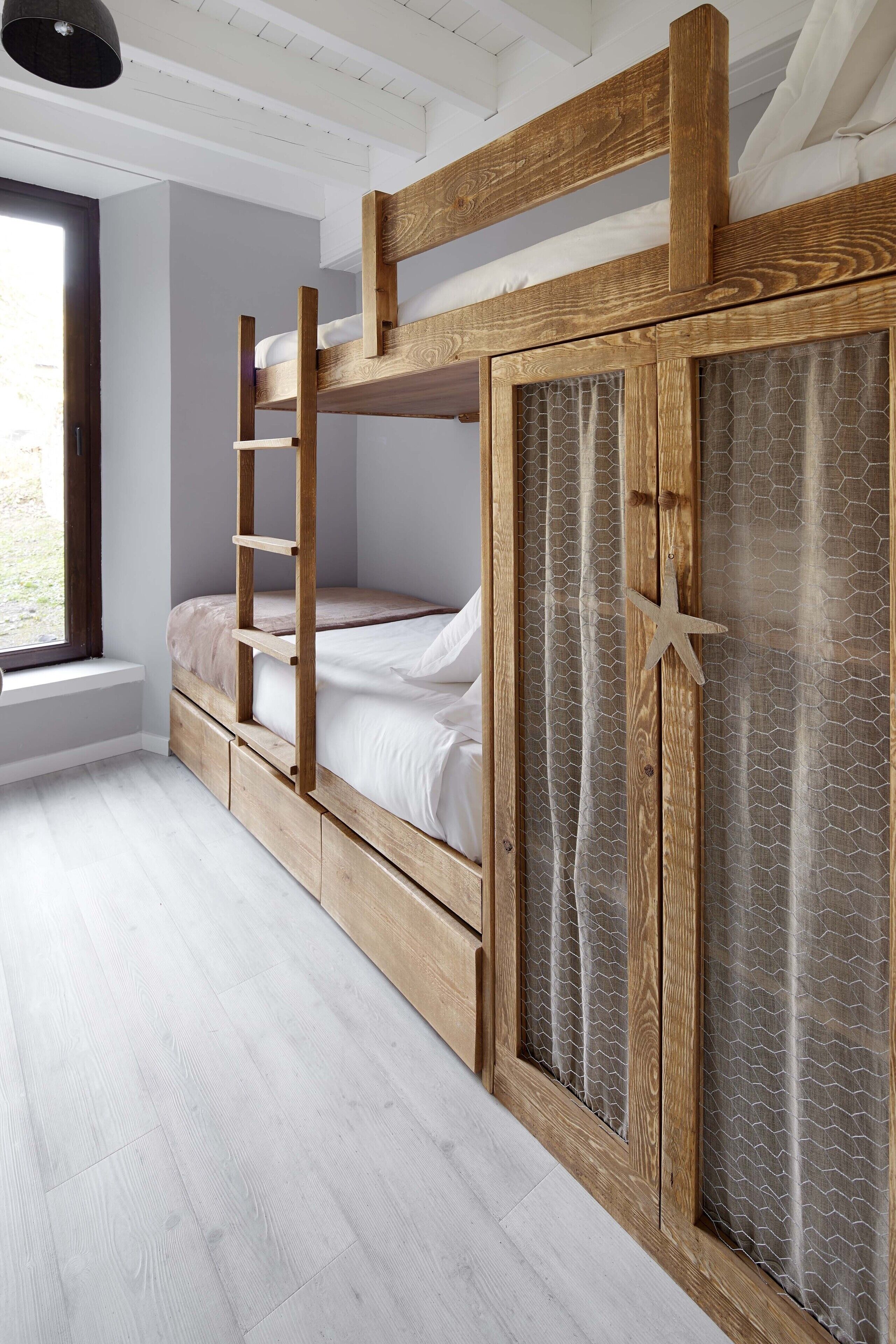 A bunk bed with a ladder, wooden wardrobe, and a window with a view.