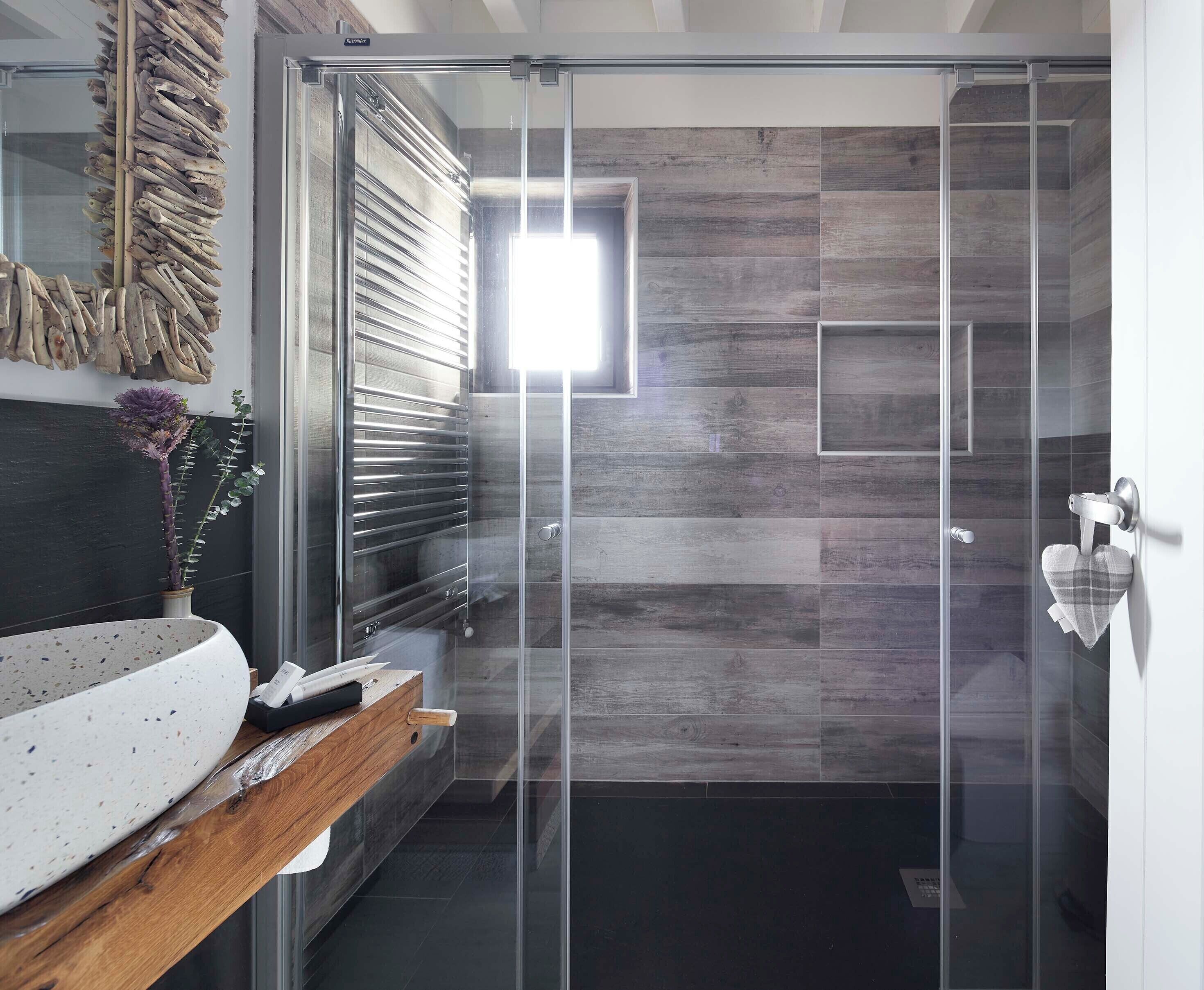 Un baño moderno con cabina de ducha de vidrio, tocador de madera y una planta decorativa.