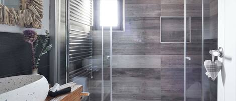 Un baño moderno con cabina de ducha de vidrio, tocador de madera y una planta decorativa.