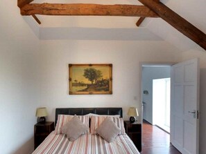 Une chambre à coucher avec un lit, deux tables de chevet, une lampe sur chacune, un tableau au mur et une poutre en bois au plafond.