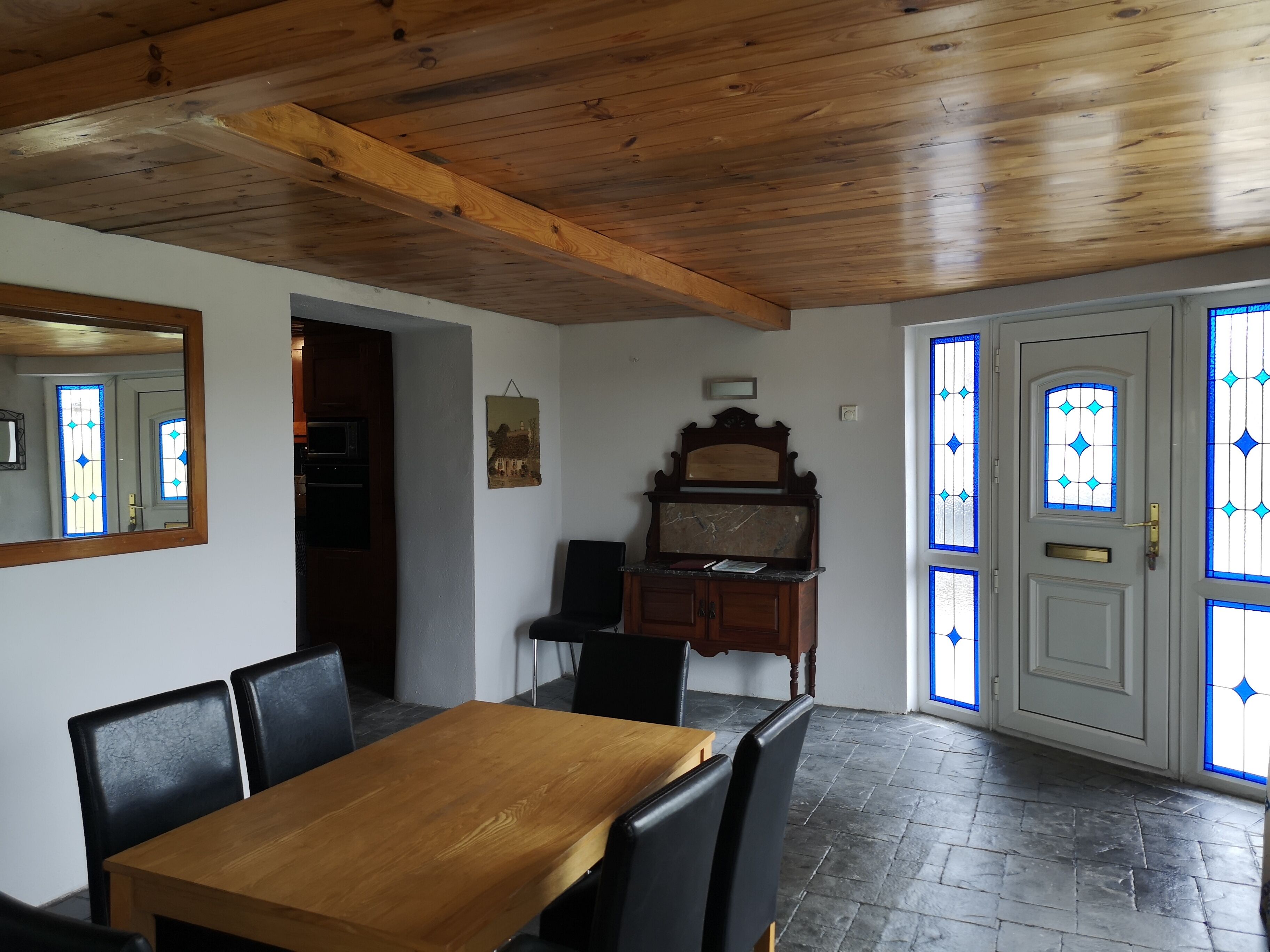 A dining area with a wooden table and chairs, a mirror, a cabinet, and a door with stained glass windows.