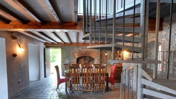 Ein rustikales Interieur mit Kamin aus Stein, Holzmöbeln und einer Wendeltreppe.