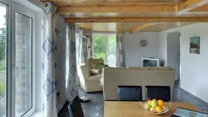 Ein gemütliches Wohnzimmer mit Holzboden, einer Couch, einem Esstisch mit Obst und einem Fernseher.
