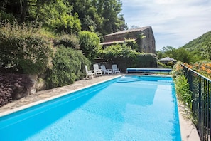 A rectangular swimming pool with clear blue water, surrounded by lush greenery and a stone wall.