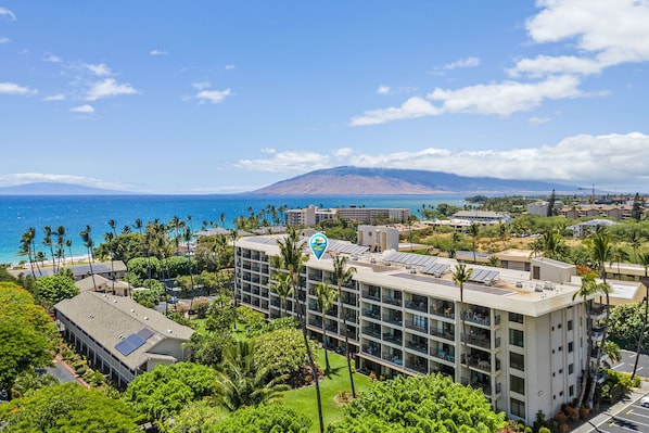 A hotel with multiple floors, solar panels on the roof, and a view of the ocean and mountains in the background.