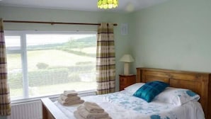 Una cama bien hecha con cubrecama floral, cabecera de madera y ventana con persianas y cortinas.