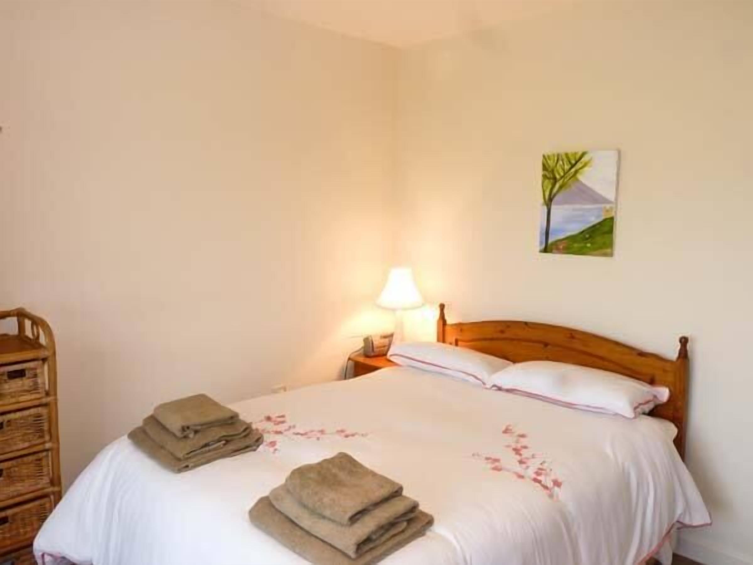 A neatly made bed with folded towels and a lamp on a bedside table.