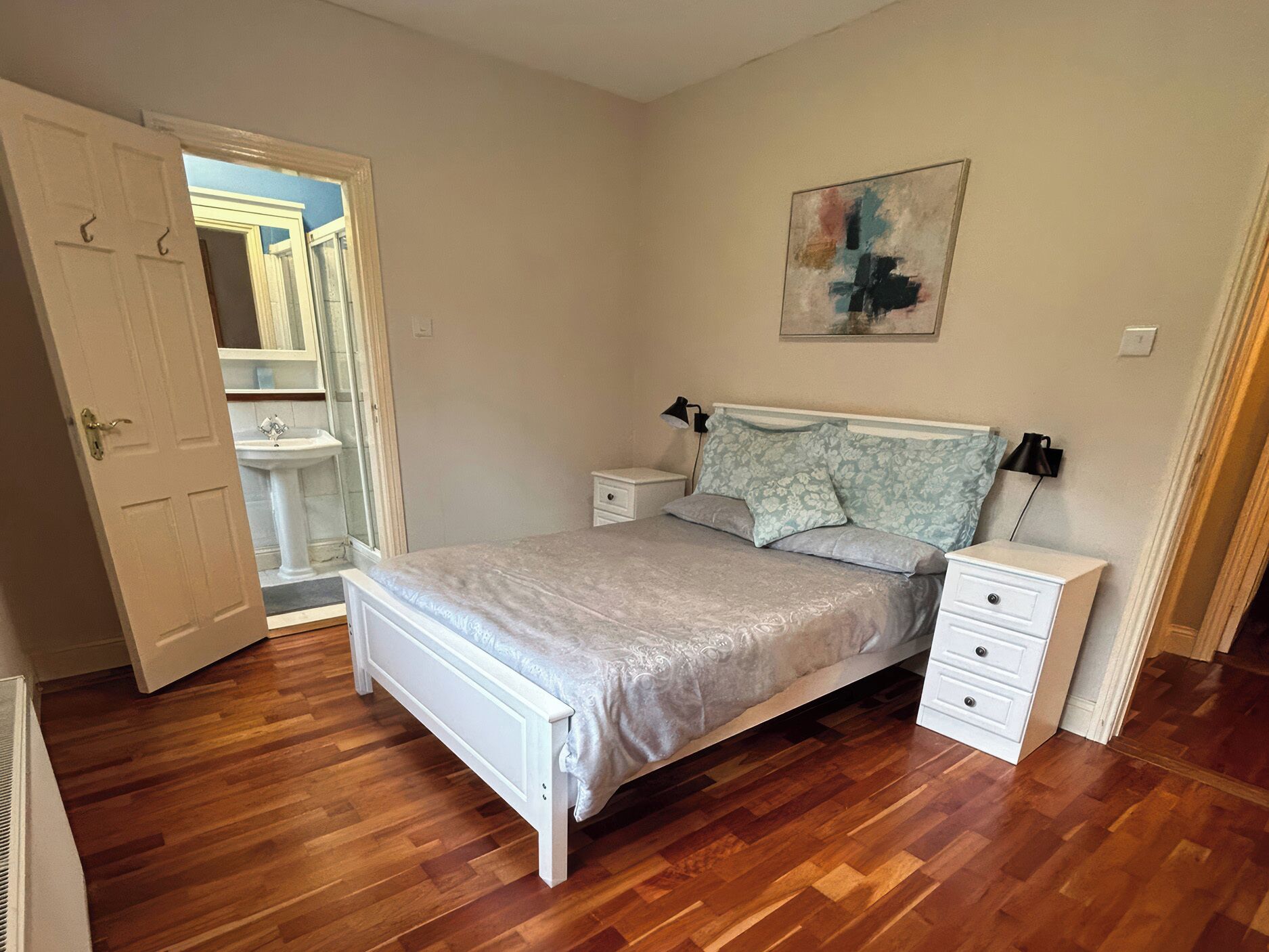 Un dormitorio con cama, mesitas de noche, lámpara de pared y un cuadro.