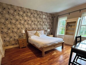 A bedroom with a wooden bed, nightstands, a window with curtains, and a bookshelf. - The Sanctuary (Churchfield)