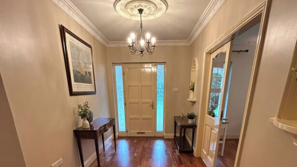 Un couloir doté d’un plancher en bois, d’un lustre, d’une porte en verre dépoli et d’un tableau encadré accroché au mur.